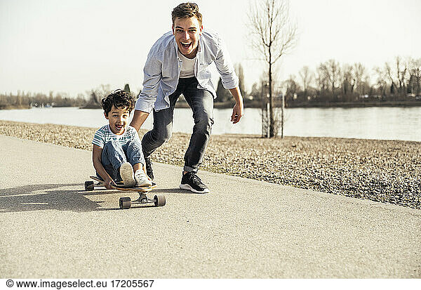 Fröhlicher Mann und Junge spielen mit Skateboard auf der Straße an einem sonnigen Tag