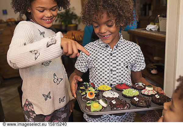 Fröhliches Geschwisterpaar mit dekorierten Halloween-Cupcakes