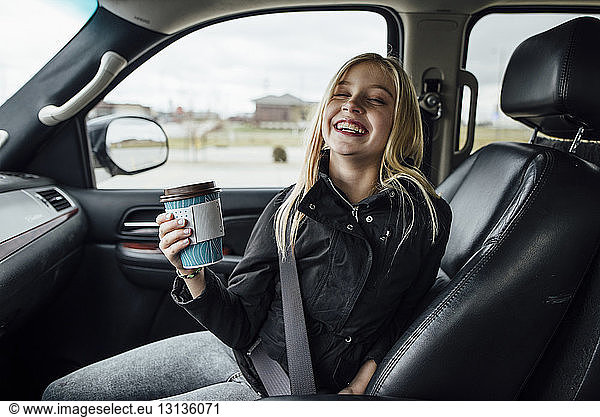 Fröhliches Mädchen hält Einwegbecher  während sie im Auto sitzt