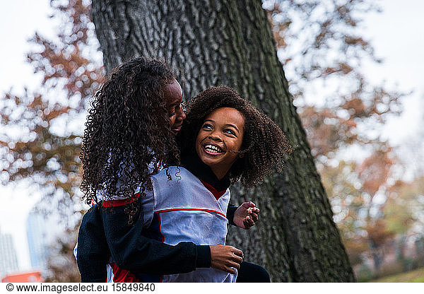 Fröhliches Mädchen mit Huckepack-Schwester im Park