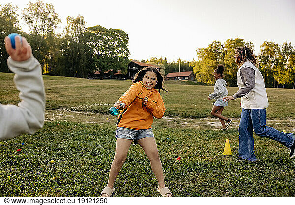 Fröhliches Mädchen spritzt mit Wasser  während es mit Freunden auf dem Spielplatz im Sommercamp spielt