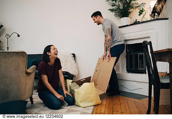 Fröhliches Paar beim Auspacken von Kisten im Wohnzimmer im neuen Zuhause