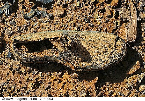 Fragment von Gummistiefel auf roter Erde  verrottete Schuhe am Boden  verrotteter Schuh  Schuhwrack  vergammelter Treter  ausgelatschter Schuh  abgetragener Schuh