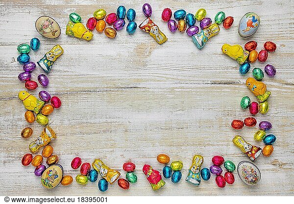 Frame of colourful Easter sweets on wood  chocolate eggs  chocolate bunnies and Easter decorations