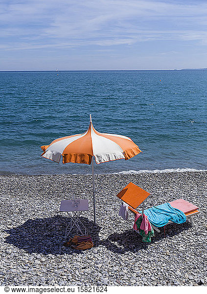 France  Alpes-Maritimes  Cagnes-sur-Mer  Beach umbrella and deck chair on rocky coastal beach with clear line of horizon over Mediterranean Sea in background