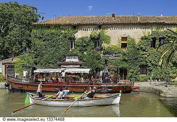 France  Aude  Saint Nazaire d'Aude  Canal du Midi listed as World Heritage by UNESCO  Port of Somail  rowers on a traditional boat passing in front of a building in murx covered with Virginia creeper