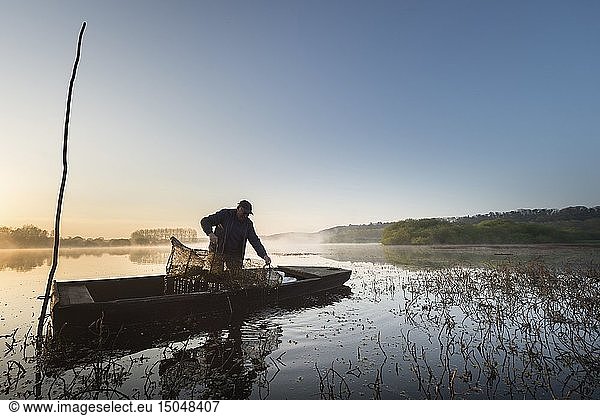 France  Morbihan  La Gacilly  Glenac marsh  fisherman in traditional boat at sunrise