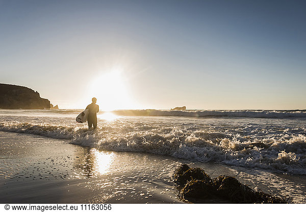 Frankreich  Bretagne  Halbinsel Crozon  Frau im Meer bei Sonnenuntergang mit Surfbrett