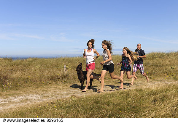 Frankreich  Bretagne  Ste Marguerite  Landeda  Finistre  Eltern und zwei Töchter  die mit ihrem Hund auf einer Düne am Atlantik laufen.