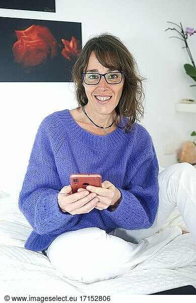 Frau am Morgen im Bett lächelnd und mit ihrem Smartphone hantierend