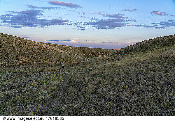 Frau auf einem Wanderweg im Grasslands National Park  Saskatchewan. Das späte Tageslicht beginnt den Himmel zu erhellen; Val Marie  Saskatchewan  Kanada