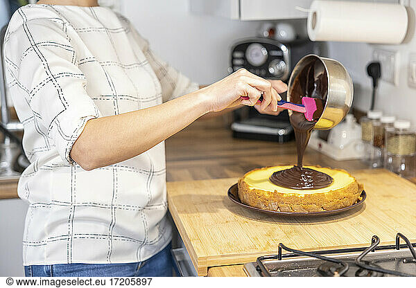 Frau backt Kuchen und bestreicht ihn mit Schokolade