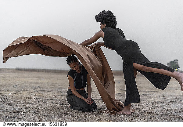 Frau bedeckt eine andere Frau mit einer Decke in trostloser Landschaft
