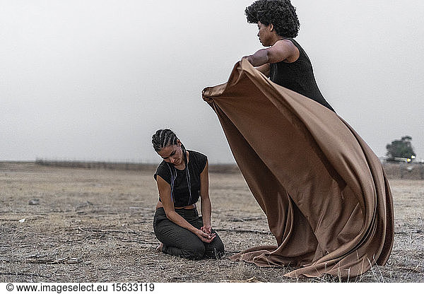 Frau bedeckt eine andere Frau mit einer Decke in trostloser Landschaft