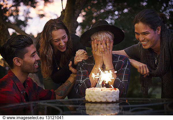Frau bedeckt ihr Gesicht  während Freunde Geburtstagskuchen anschauen