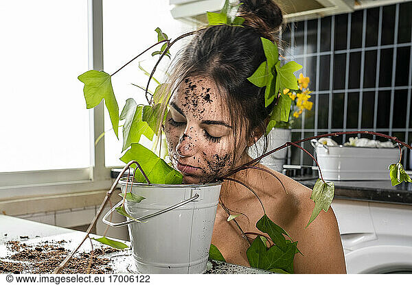 Frau bedeckt mit Pflanzenblatt riechenden Topfpflanze Schlamm zu Hause