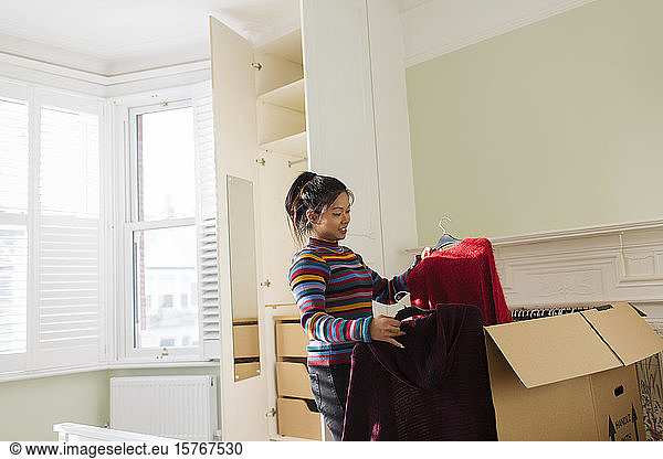 Frau beim Auspacken von Kleidung aus einem Umzugskarton im Schlafzimmer