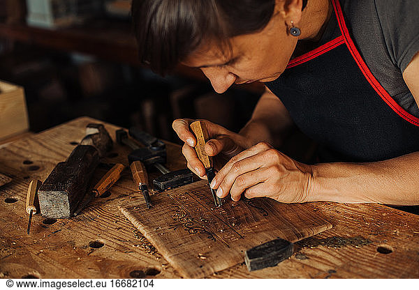 Frau beim Gravieren einer Holztafel mit Handwerkzeugen