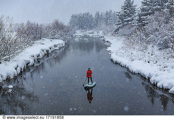 Frau beim Stand Up Paddleboarding auf einem Fluss im Winter