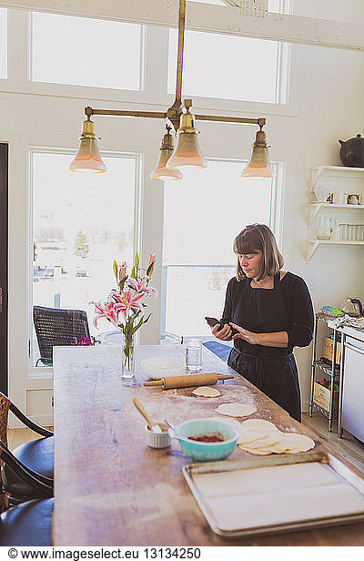 Frau benutzt Smartphone beim Zubereiten von Essen zu Hause