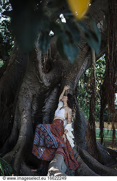 Frau berührt Baum  während sie unter einem Baum im Park sitzt