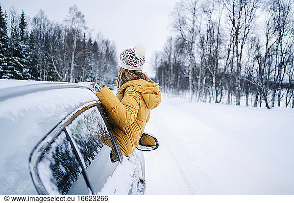 Frau betrachtet kahle Bäume  während sie sich im Winter aus dem Autofenster lehnt