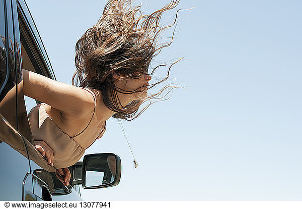 Frau beugt sich aus Autofenster gegen klaren Himmel