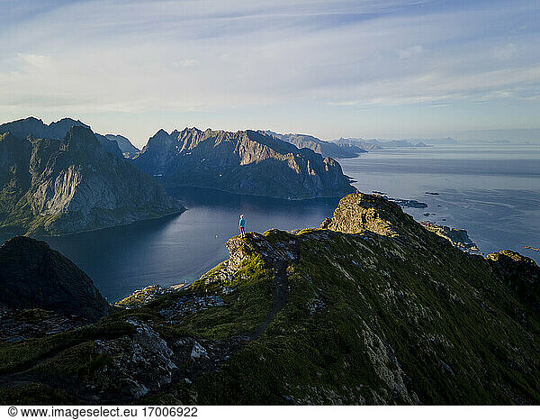 Frau bewundert die Aussicht auf die Berge  während sie auf einem Berg in Reine  Lofoten  Norwegen  steht