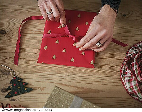Frau bindet rote Schleife an Geschenk über Tisch während Weihnachten