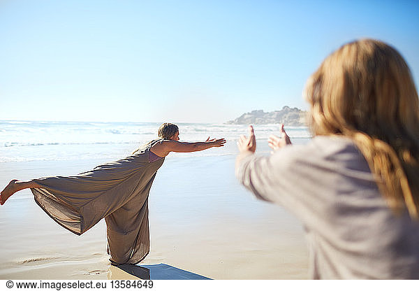 Frau übt Krieger 3 Pose am sonnigen Strand während Yoga-Retreat