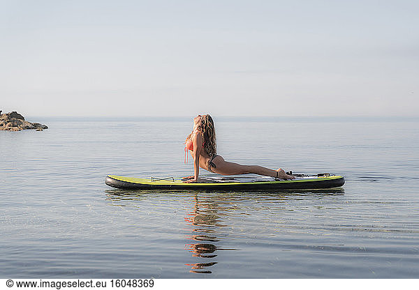 Frau übt nach oben gerichteten Hund Position auf Paddleboard über Meer gegen den Himmel