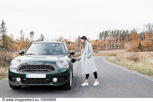 Frau  die auf dem Land ihr Elektroauto Mini Countryman einsteckt