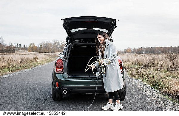 Frau  die ein Ladegerät für ein Elektroauto in den Kofferraum ihres Autos legt
