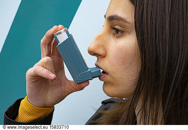 Frau  die einen blauen Asthma-Inhalator auf blauem Hintergrund inhaliert.