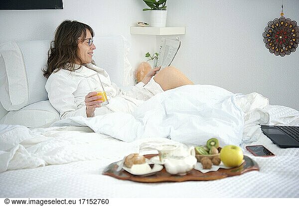 Frau  die im Bett frühstückt und eine Zeitung liest