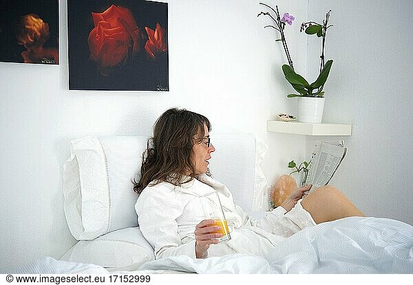 Frau  die im Bett frühstückt und eine Zeitung liest