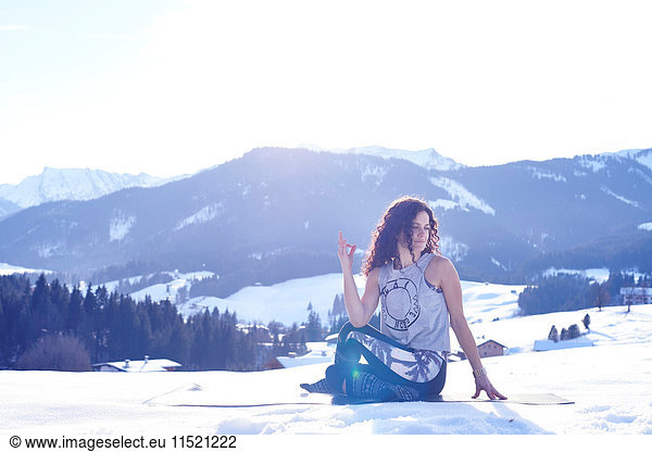 Frau  die in verschneiter  sonnenbeschienener Landschaft eine weise Yogastellung einnimmt  Österreich