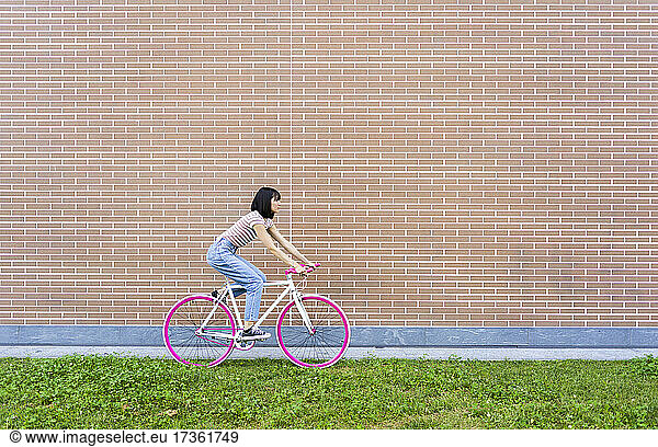 Frau fährt mit dem Fahrrad an einer Backsteinmauer vorbei