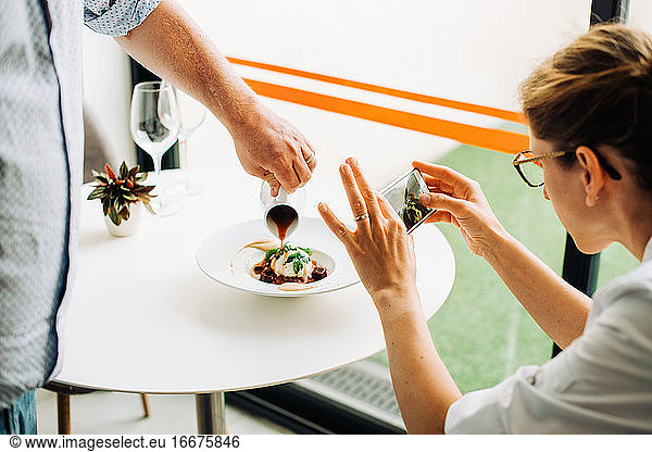 Frau fotografiert Essen mit Smartphone  während der Kellner das Essen serviert