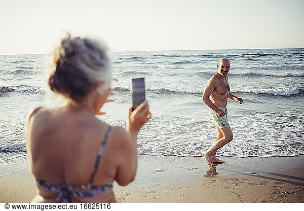 Frau fotografiert Mann beim Laufen am Strand