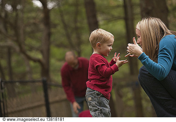 Frau gebärdet das Wort ´Play´ in amerikanischer Zeichensprache  während sie mit ihrem Sohn in einem Park kommuniziert