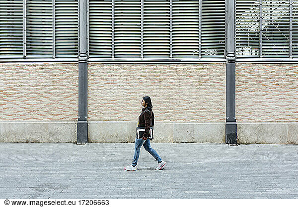 Frau geht auf dem Gehweg an einem Gebäude vorbei und schaut weg