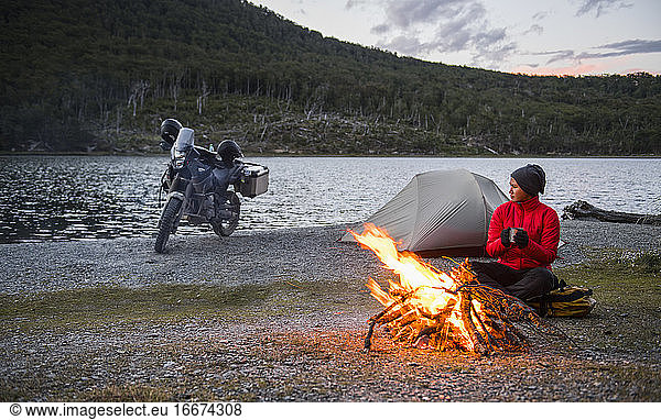 Frau genießt das Lagerfeuer im Camp neben einem stillen See in Feuerland