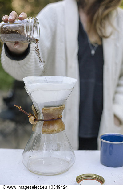 Frau gießt gemahlenen Kaffee aus einem Glas in eine Glas-Kaffeemaschine.