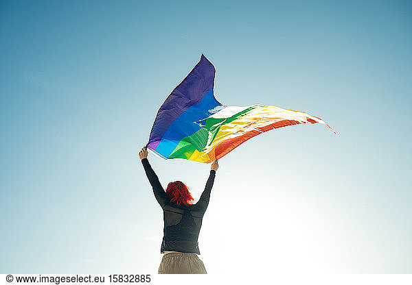 Frau hält die schwule Regenbogenfahne auf blauem Himmelshintergrund. Glück  Freiheit und Liebeskonzept für gleichgeschlechtliche Paare.