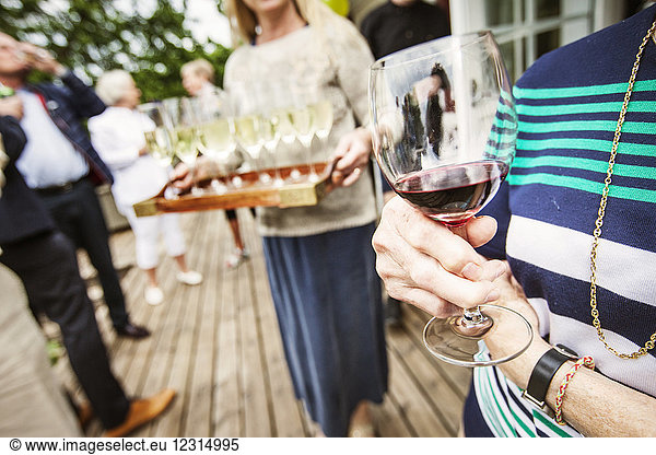 Frau hält ein Glas Rotwein bei einer Gartenparty