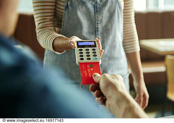 Frau hält kontaktloses Zahlungsterminal für einen Kunden  der mit Karte bezahlt
