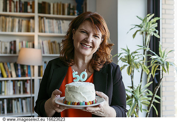 Frau hält Kuchen mit Kerze Nummer 50  während sie zu Hause steht