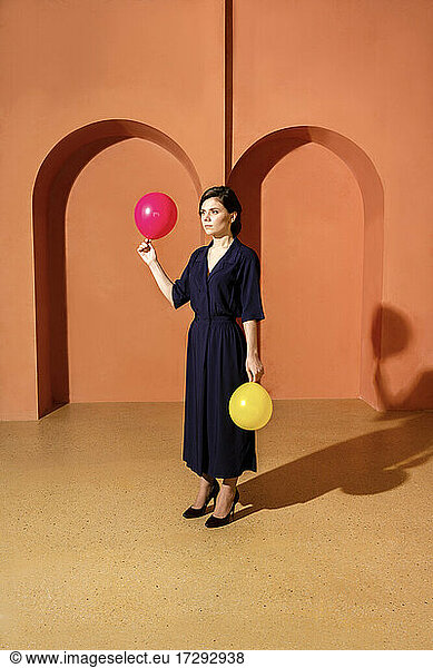 Frau hält Luftballons vor einer Mauer mit Bögen