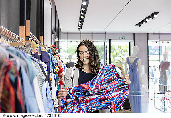 Frau hält mehrfarbiges Kleid beim Einkaufen in einer Boutique